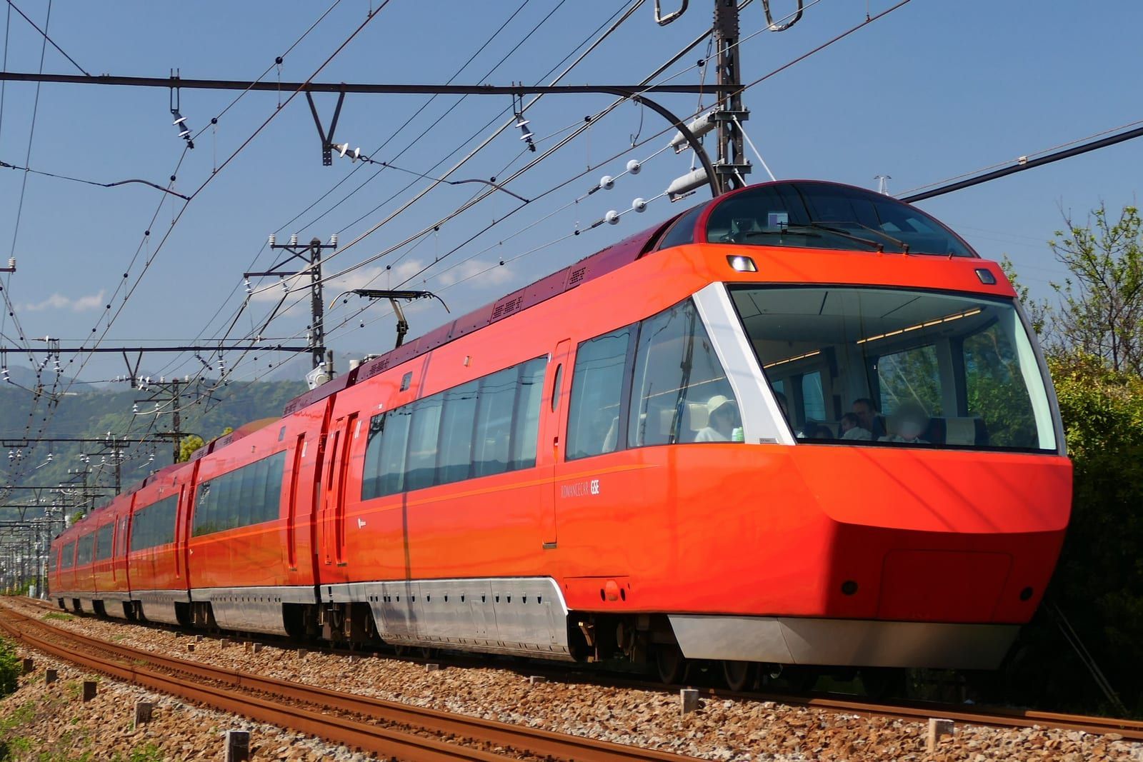 A red Odakyu Romancecar limited express running along the Odawara Line under a blue sky