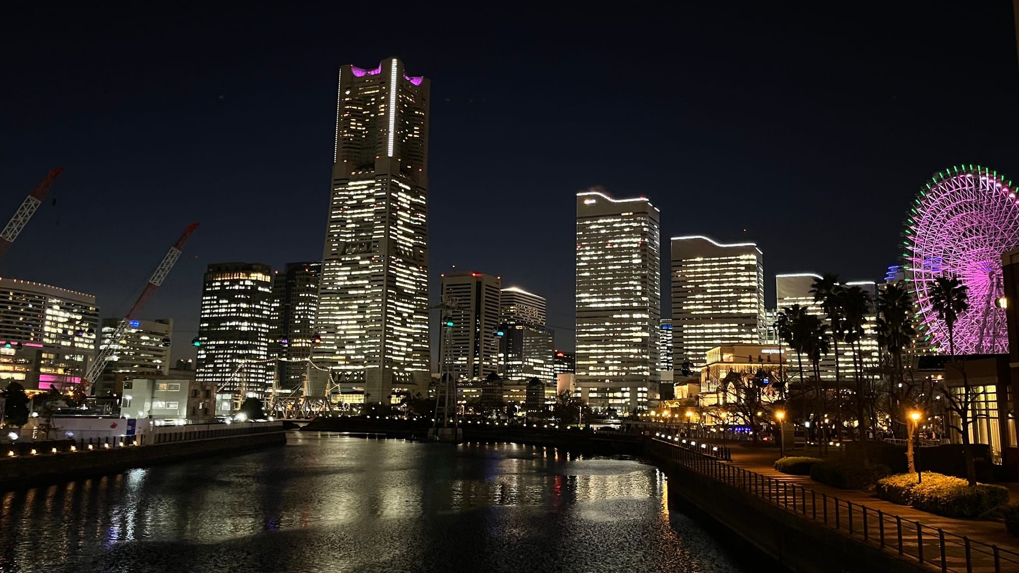 Landmark Tower and the lit Cosmo Clock 21 Ferris wheel at night, reflected in the water of the old dock by the Yokohama Port Museum